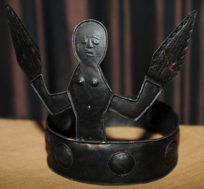 Description: Metal headdress with an anthropomorphic figure with raised arms. Timor Leste